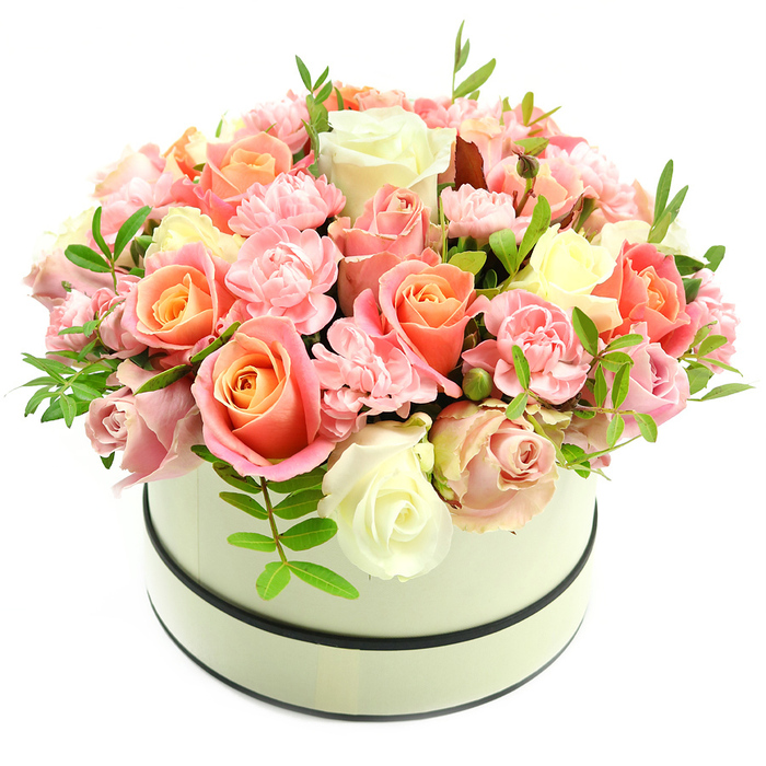 A refined, luxurious hatbox arrangement presented with attentive craftsmanship: the composition forms a lush, domed volume of blooms that command attention while remaining quietly elegant. The palette is soft and romantic - roses in abundant variety show warm coral-peach and apricot tones at their cores gently fading to blush pink and creamy ivory at the petal margins, creating subtle, painterly gradations. Interspersed among the larger roses are numerous frilly light-pink carnations that add tactile detail and a plush, layered texture to the bouquet. Occasional sprigs of vivid green foliage rise between the flowers, their narrow leaves giving the arrangement breathing space and a fresh counterpoint to the rosy hues. The flowers sit in a round, matte cream hatbox with two thin dark bands, one circling the top rim and one near the base, lending a classic, restrained contrast that emphasises the arrangement's silhouette. Photographed on a stark white background with soft, flattering light, each petal's velvety surface and fine veining are visible, and the overall impression is one of sumptuous, contemporary elegance. This piece suits formal celebrations and intimate gestures alike - an elevated gift for anniversaries, Mother's Day, or to mark a milestone with dignity and warmth. For clients in Chessington, Surbiton, and the surrounding towns, this composition translates floral expertise into a tactile, fragrant statement of affection and refined taste.