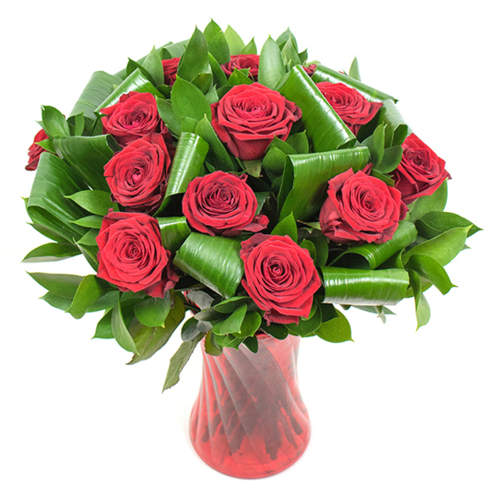 Here a dozen-plus deep crimson roses command attention, each bloom perfectly open and plush, their velvet-like petals layered in rich spirals that catch the light and read as intense, romantic red. The rose heads are surrounded and supported by abundant dark green foliage: narrower, glossy leaves form a dense, natural backdrop while larger, bright green leaves have been artfully folded and rolled into cylindrical curls and graceful loops that cradle the blooms and add structural drama. The whole composition sits in a tall, slender translucent ruby red vase, its subtle twisted or ribbed glass producing vertical highlights and delicate reflections that echo the roses' depth and lend a contemporary sensibility to the classic bouquet. Bathed in soft, even lighting against a clean white canvas, the contrasts between the crimson blooms and the verdant greens are crisp and immediate, emphasising texture, volume and careful floral technique. The scent is implied-a gentle, unmistakable rose fragrance-and there is a pleasing contrast between the soft, tender petals and the cool smoothness of the glass vessel. This arrangement radiates timeless romance and refined taste, ideal for anniversaries, Valentine's moments, or as a striking centrepiece at a romantic dinner. Crafted with neighbourhood sensibilities, this style is part of our signature offerings for customers across Chessington and nearby Surbiton or Kingston; Chessington Flowers often prepares similarly composed bouquets for same-day delivery when freshness and thoughtful presentation matter most.