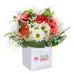 There's a cheerful exuberance in this Chessington bouquet, artfully perched within a square white gift bag, its sturdy ribbon handles ready for an effortless delivery. The playful blend of coral, peach, and striking red carnations brings warmth and vibrancy, their frilled petals unfurling like the blooms of early spring along the Chessington trails. Radiant white daisies with bright yellow-green centers punctuate the display, their crispness recalling the pure joy of sun-kissed wildflowers in local woods. Wispy sprays of baby's breath float through the arrangement, enhancing its softness and conveying gentle, heartfelt care. At the bouquet's edge, hints of unopened buds dusted with purple suggest a story still unfolding-a subtle nod to the seasons changing in Chessington's leafy lanes. Deep green, glossy foliage encircles the base, providing a rich backdrop and a final touch of craftsmanship. Against a stark white background, each detail is illuminated-every petal, every leaf, and every nuance in between-embodying freshness and the joy of thoughtful floristry. Whether it's a birthday gift, a spontaneous pick-me-up sent across Chessington, or a way to brighten a loved one's day, this arrangement is a testament to local expertise and the simple pleasures of giving.